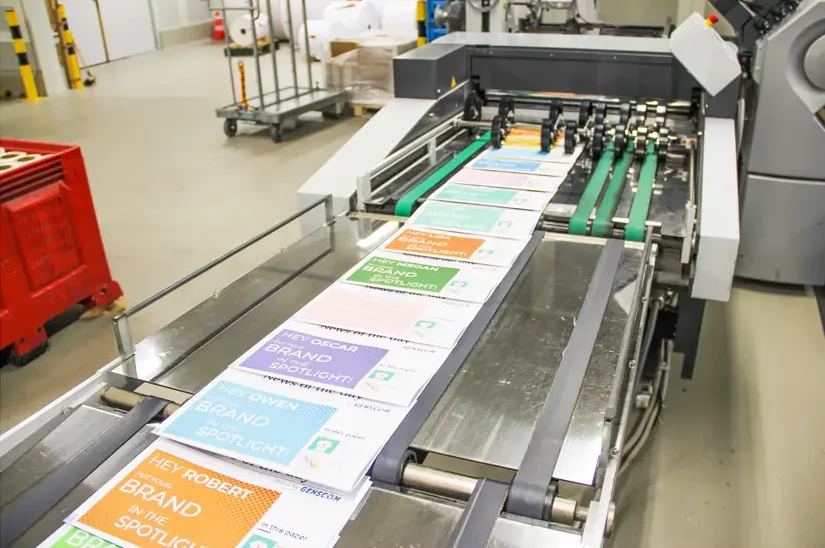 Geautomatiseerde afwerkingslijn verwerkt opeenvolgende gepersonaliseerde kranten met unieke inhoud, klaar voor verzending.