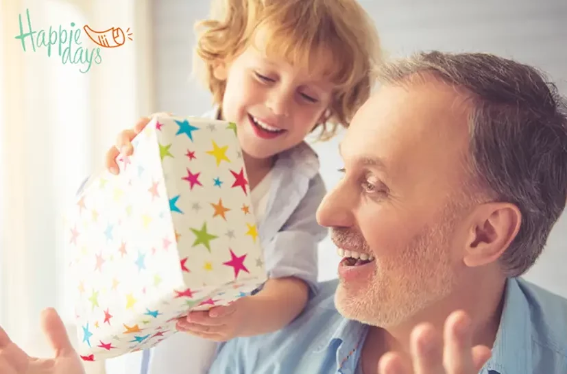 Kind en volwassene glimlachen terwijl een kleurrijk ingepakt cadeau wordt overhandigd tijdens een feestelijk moment. happiedays logo staat linksbovenaan
