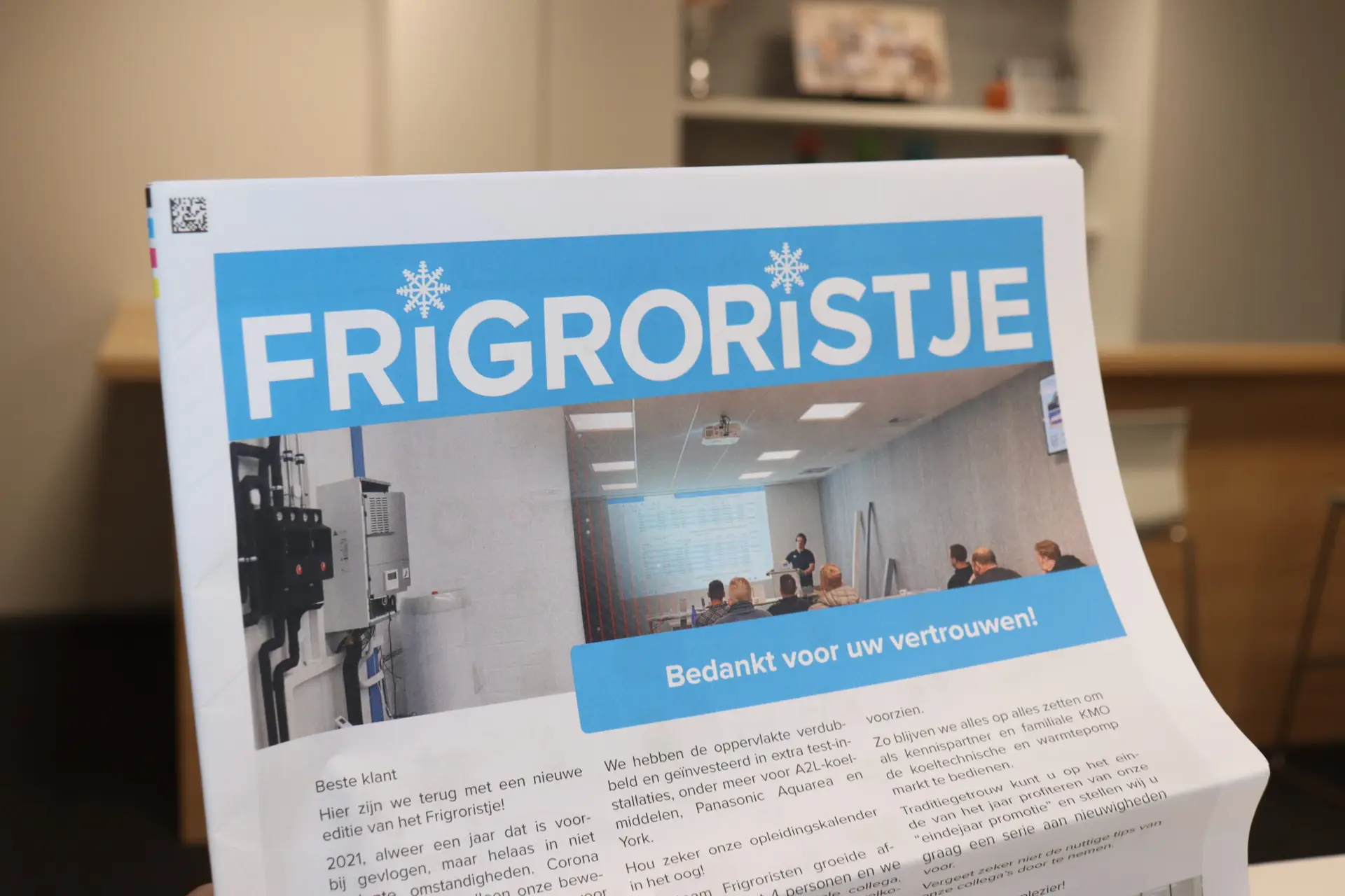 Close-up van een gepersonaliseerde personeelskrant met een professionele voorpagina, vastgehouden in een kantooromgeving.